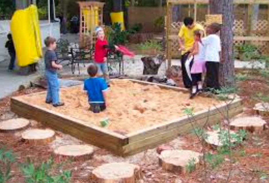 5 children and a parent playing in a sandbox outdoors.
